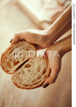 Perfect French breakfast, lunch, snack. Close up image of baker's hands hold cut croissant and show how perfectly cooked it is. 110057737