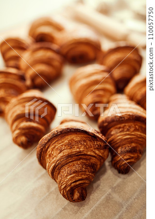Close up photo of group of croissants with golden brown color and have flaky, buttery crust, sitting on top of white paper bag on table. Close up photo of group of croissants with golden brown color and have flaky, buttery crust, sitting on top of white paper bag on table. 110057750
