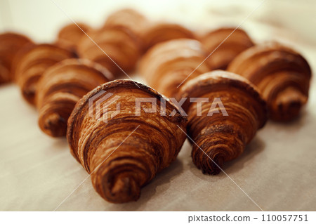 Close up photo of plate of golden brown, freshly baked, hot, delicious pastries, French croissants sitting on table covered with bakery parchment. 110057751