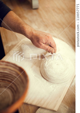 Person making dough on wooden cutting board. white and well-floured pastry. Hand gently pressing down on dough, and fingers spread out. Person making dough on wooden cutting board. white and well-floured pastry. Hand gently pressing down on dough, and fingers spread out. 110057771