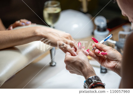 Close-up shot of a woman hand in a nail salon receiving manicure by beautician with brush. Woman getting nail manicure at spa centre. 110057960