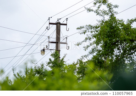 Old electricity power supply pillar. Power line post with electric cables against a clear sky. A trees grows around  110057965