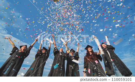 Graduates throw colorful confetti against a blue sky. 110059101
