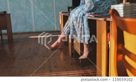 The girl moves her legs sitting on the table. 110059102