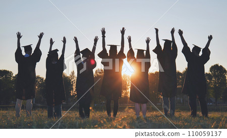 College graduates in robes waving at sunset. 110059137