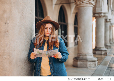 Pretty young woman staying on the street holding paper map in hands. 30s girl in hat posing on Market Square in Krakow. Traveling Europe, High quality photo, The Cloth Hall, Vacation concept Pretty young woman staying on the street holding paper map in hands. 30s girl in hat posing on Market Square in Krakow. Traveling Europe, High quality photo, The Cloth Hall, Vacation concept 110060085