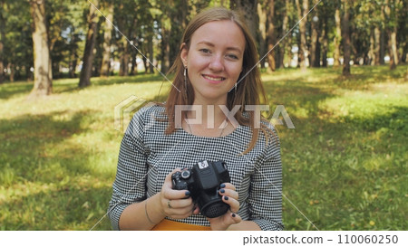A young girl photographer with a camera poses in the park. 110060250