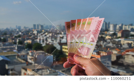 Man's Hand holding rupiah money against the backdrop of the capital of Indonesia. Man's Hand holding rupiah money against the backdrop of the capital of Indonesia. 110060251