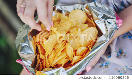 A girl eating chips on a summer afternoon. A pack of chips in close-up. 110060266