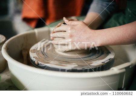 Close-up of a woman hands moulding a ceramic piece on the potter's wheel Creating a ceramic mould from clay in potters workshop Close-up of a woman hands moulding a ceramic piece on the potter's wheel Creating a ceramic mould from clay in potters workshop 110060682