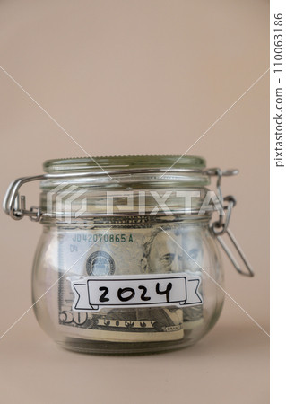 Saving Money In Glass Jar filled with Dollars banknotes. 2024 year transcription in front of jar. Managing personal finances extra income for future insecurity Saving Money In Glass Jar filled with Dollars banknotes. 2024 year transcription in front of jar. Managing personal finances extra income for future insecurity 110063186