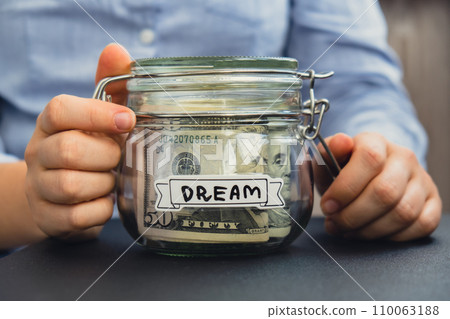 Female hands holding Glass jar full of American currency dollars cash banknote with text DREAM. Preparation saving money. Moderate consumption and economy 110063188