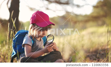 child girl boy scout studying a pine cone in the forest with a magnifying glass. happy family child lifestyle dream concept. child tourist explorer with magnifying glass in the forest child girl boy scout studying a pine cone in the forest with a magnifying glass. happy family child lifestyle dream concept. child tourist explorer with magnifying glass in the forest 110063356