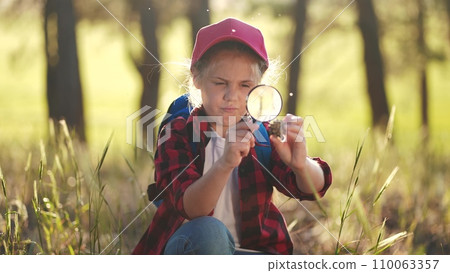 child girl boy scout studying a pine cone in the forest with a magnifying glass. happy family child dream concept. child tourist explorer with magnifying lifestyle glass in the forest 110063357