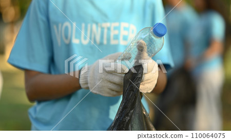 Cropped shot of female volunteer collecting garbage in public park. Charity and ecology concept. Cropped shot of female volunteer collecting garbage in public park. Charity and ecology concept. 110064075