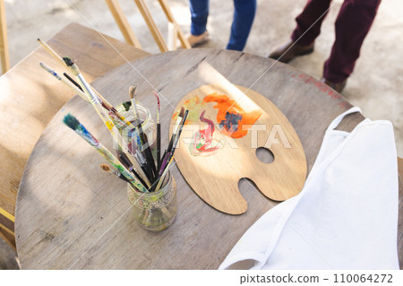 Close up of paints and jars with brushes on wooden table on sunny terrace 110064272