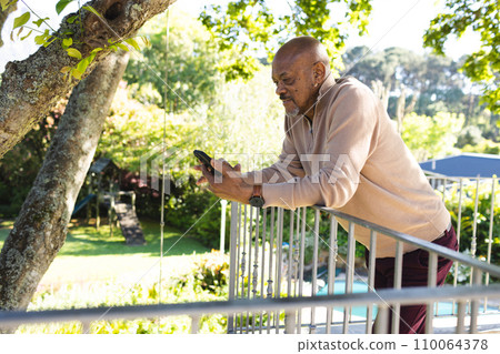 African american senior man using smartphone on sunny terrace 110064378