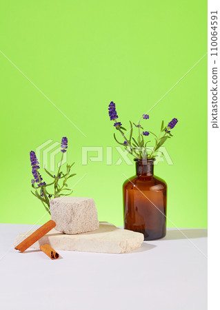 Lavender flowers are inserted in a brown vase, cinnamon and a stone platform are displayed on a white table with a blue background. Display products in a sophisticated space. 110064591