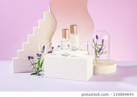 A perfume bottle on a white podium is reflected in a mirror, surrounded by lavender flowers on a light purple background. Mockup for perfume advertising. 110064643