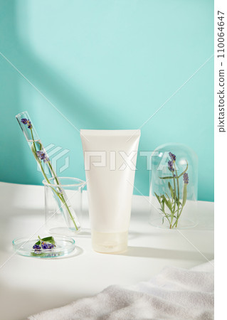 Close-up of an unlabeled cosmetic tube with lavender flowers stored in glassware. Delicate blue and white background. Cosmetic mockup for advertising. 110064647