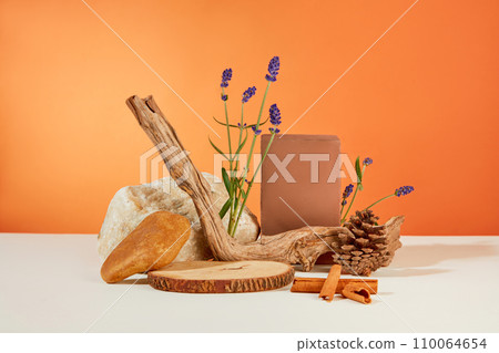 The front of the wooden platforms, stone slabs, cinnamon and lavender flowers are displayed on an orange-white background. Scene for natural cosmetics advertising. The front of the wooden platforms, stone slabs, cinnamon and lavender flowers are displayed on an orange-white background. Scene for natural cosmetics advertising. 110064654