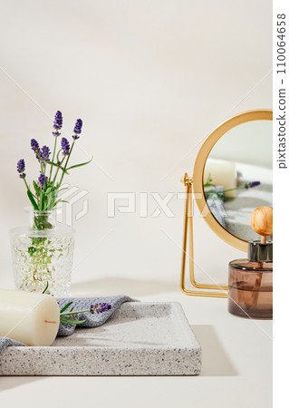 Lavender flowers inside a glass vase on a gray tray with candles and towels, and a diffuser of essential oils is placed next to a mirror on a white background. Natural fragrance. 110064658