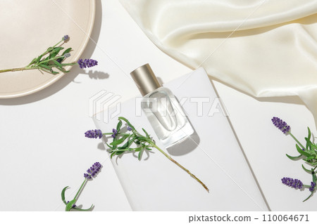 A bottle of unbranded perfume is displayed on a white podium alongside lavender flowers. Lavender can help reduce stress, anxiety, insomnia and depression. A bottle of unbranded perfume is displayed on a white podium alongside lavender flowers. Lavender can help reduce stress, anxiety, insomnia and depression. 110064671