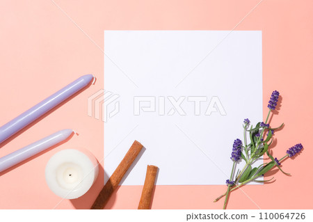 A white square on a pink background, surrounded by candles, scented candles, cinnamon and lavender flowers. Empty space for product display. Flat lay. 110064726