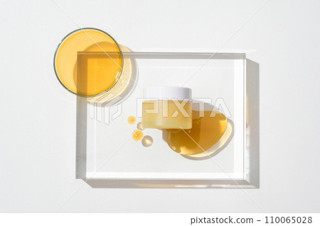 Close-up of a jar of unbranded cosmetics displayed on a transparent glass platform with drops of honey. Honey is used as a very good skin moisturizer. 110065028