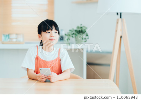 An elementary school girl operates a smartphone in the living room. 110065948