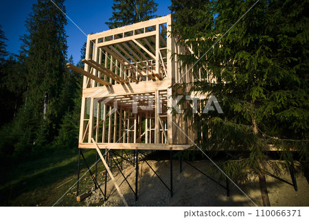 Drone's vantage point offers view of two-storey wooden-framed domicile in process of construction near forest. Idea of contemporary ecological construction and modern architectural design. Drone's vantage point offers view of two-storey wooden-framed domicile in process of construction near forest. Idea of contemporary ecological construction and modern architectural design. 110066371