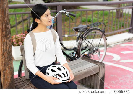 Young woman resting on a bench with a cycling helmet on her lap Young woman resting on a bench with a cycling helmet on her lap 110066875