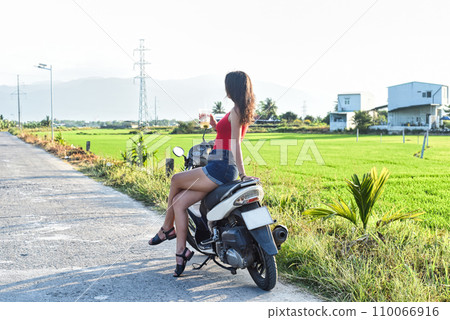 Young woman drives a motorbike among rice fields in Vietnam 110066916