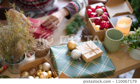 Young asian woman in sweater wrapping christmas gift and decorating with hemp rope while preparing toys ornaments and presents to celebrate for christmas festive holiday and winter seasons at house 110067179