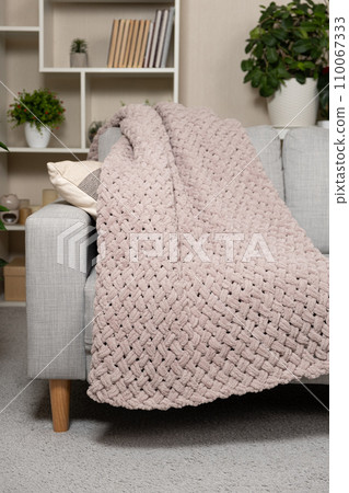 Knitted large plaid blanket in dusty rose light grayish-red color on the sofa. 110067333