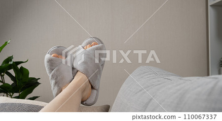 Stylish modern grey house slippers on women's feet lying on sofa. Copy space for text Stylish modern grey house slippers on women's feet lying on sofa. Copy space for text 110067337