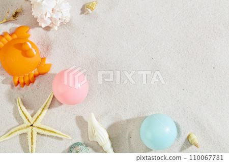 Colorful plastic balls, seashells and a silicone crab are decorated on a smooth sand background. Free space for product display, typography and more. Sea vibes. 110067781