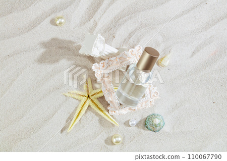 Close-up of an unbranded perfume bottle decorated with sea shells, pearls and ornaments on a sandy background. The fresh scent brings a vibrant summer mood. 110067790