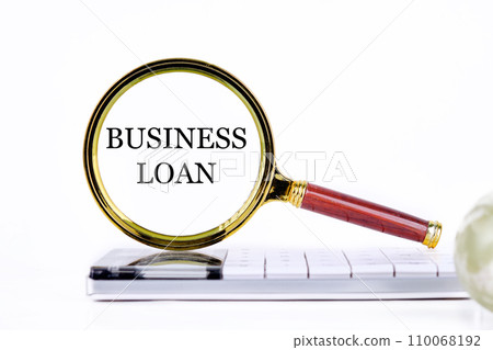 BUSINESS LOAN lettering through a magnifying glass on a calculator and part of a magic ball in the foreground without focus 110068192