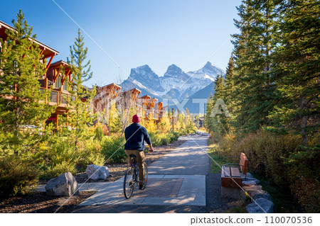 People riding a bicycle on walking trail in residential area. Town of Canmore street view in fall season. Alberta, Canada. People riding a bicycle on walking trail in residential area. Town of Canmore street view in fall season. Alberta, Canada. 110070536