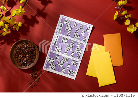 Flat lay of a plate of melon seeds, a lottery sheet, lucky money envelope and yellow apricot flower branch on a red background. Festive atmosphere. 110071119