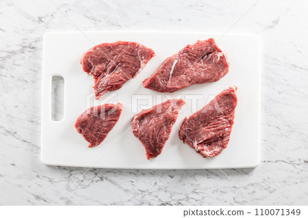 Raw fresh beef meat cut into steaks on a white cutting board - Top of view. Raw fresh beef meat cut into steaks on a white cutting board - Top of view. 110071349