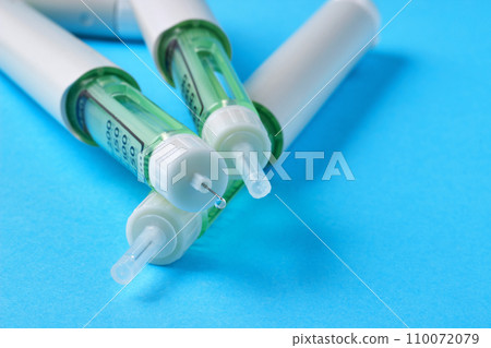 Insulin syringe pen with a drop of medicine at the end of the needle on a blue background 110072079