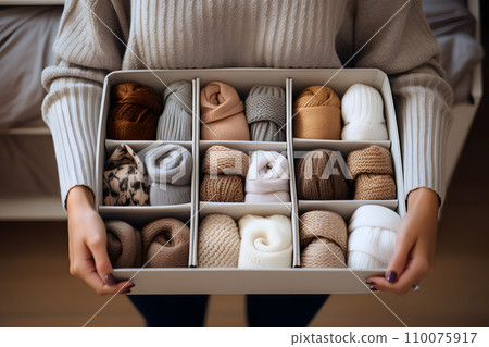 A box with dividers for categorized storage with beige-colored clothes in the woman hands 110075917