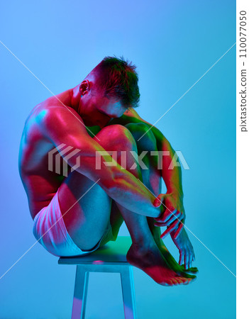 Muscular shirtless young man with relief, strong, fit shirtless body posing in underwear, boxers against gradient blue studio background in neon light Muscular shirtless young man with relief, strong, fit shirtless body posing in underwear, boxers against gradient blue studio background in neon light 110077050