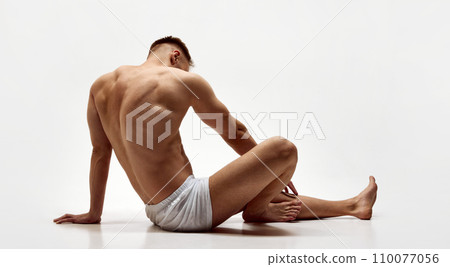 Rear view of young muscular man with relief body, strong back sitting shirtless in boxers isolated over white studio background Rear view of young muscular man with relief body, strong back sitting shirtless in boxers isolated over white studio background 110077056