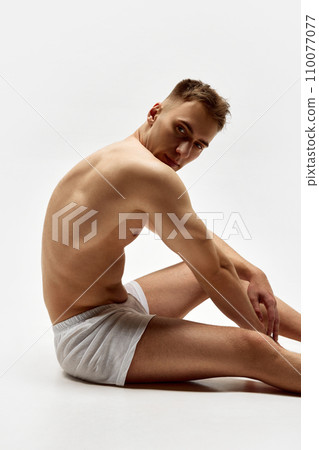 Shirtless young man with fit, sportive, relief body shape sitting on boxers, underwear isolated over white studio background Shirtless young man with fit, sportive, relief body shape sitting on boxers, underwear isolated over white studio background 110077077