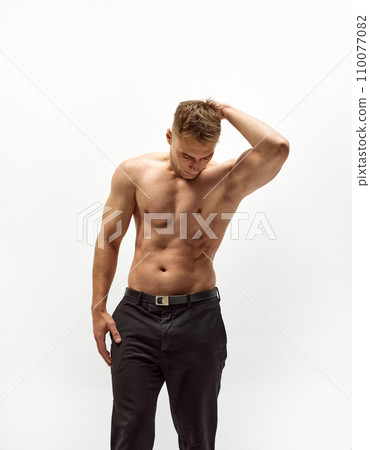 Handsome young man with shirtless, muscular body standing in pants isolated over white studio background. Relief torso Handsome young man with shirtless, muscular body standing in pants isolated over white studio background. Relief torso 110077082