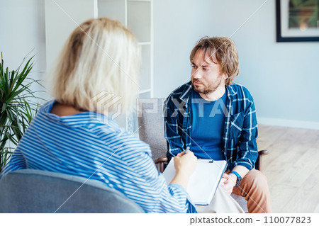 Depressed male patient having psychotherapy session with counselor at mental health clinic. Man with emotional problems consulting professional therapist i comfy office. Psychological help service. 110077823