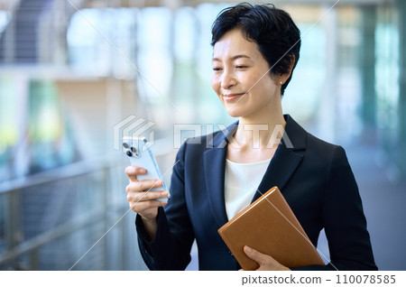 Middle business woman in a suit standing with a smartphone in the office corridor Middle business woman in a suit standing with a smartphone in the office corridor 110078585